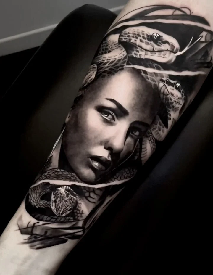 Black and grey Medusa with snakes coiled around her on the forearm